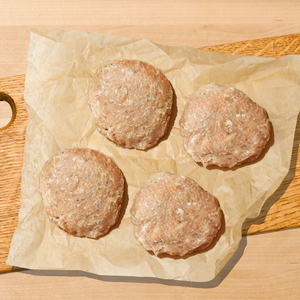 Four raw meat patties on a wooden cutting board with parchment paper