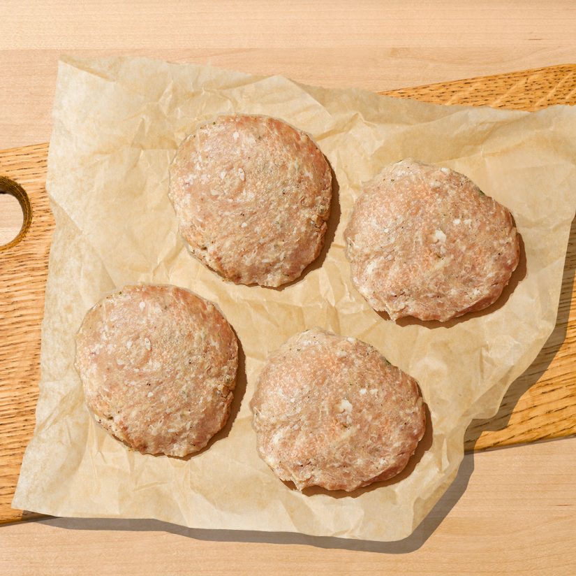 Four raw meat patties on a wooden cutting board with parchment paper